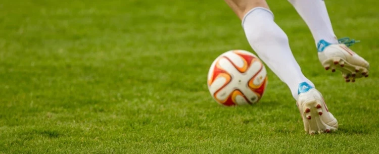 piernas de un jugador corriendo detrás de una pelota en una cancha de fútbol.